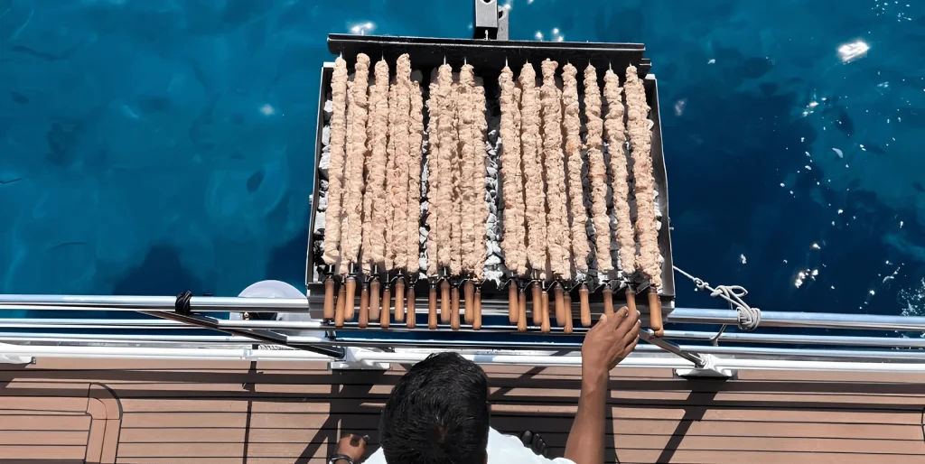 Rows of chicken souvlaki grilling on the BBQ over the sea on a SCUBACAT cruise